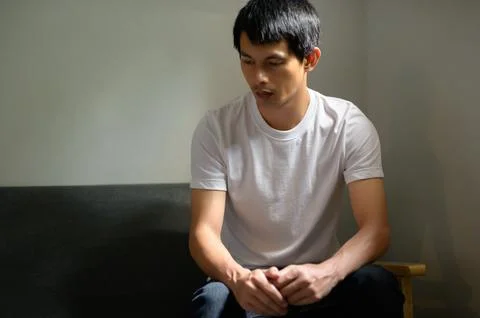 Reflective Young Man Sitting on Couch in Minimalist Interior Space Stock Photos