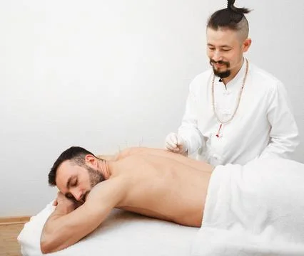 Reflexologist doing an acupuncture procedure for man with pain in his back. A Foto stock