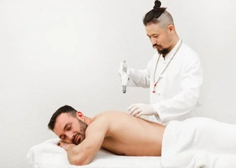 Reflexologist placing vacuum cups on the back of male patient. Traditional or Foto stock