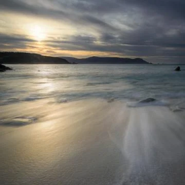 Reflow of the waves in a quiet beach at sunset Stock Photos