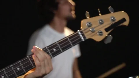 Refocus with the fingerboard of a bass guitar on a drummer with curly hair that Stock Footage