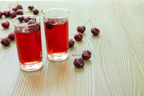 Refreshing cherry juice served in clear glasses on a light wooden table Stock Photos