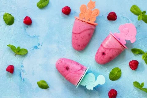 Refreshing children's ice cream popsicles (rasberry sorbet) on blue concrete Stock Photos