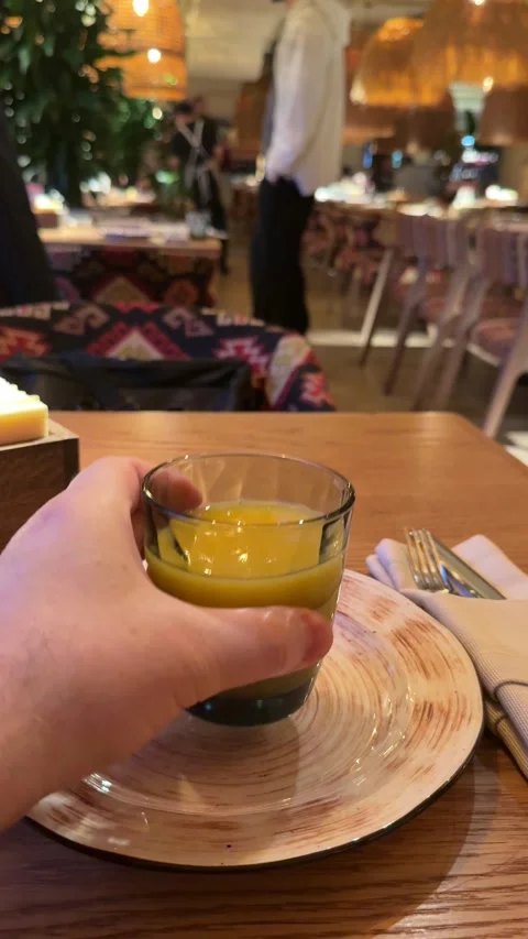 Refreshing Citrus Drink On Cozy Table, Small Glass Of Juice Amidst Warm Bistro Stock Footage 325223524