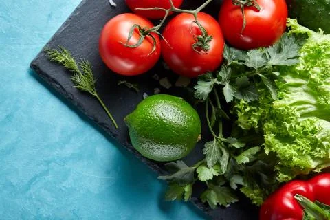 Refreshing close-up still life of assorted fresh vegetables and herbs on blue Stock Photos