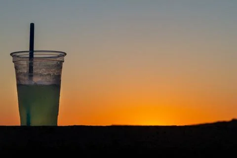Refreshing cocktail in a plastic cup, captured against a vibrant beach sunset. Stock Photos