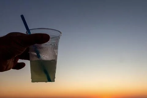 Refreshing cocktail in a plastic cup captured against a vibrant beach sunset. Stock Photos
