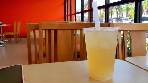 Refreshing Cold Orange Iced Drink in Transparent Plastic Cup on Cafe Table Stock Footage 320291426
