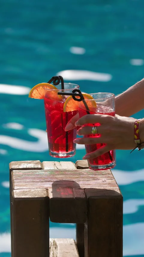 Refreshing drinks in a glasses near swimming pool. Woman puts two red cocktails Stock Footage 314564510