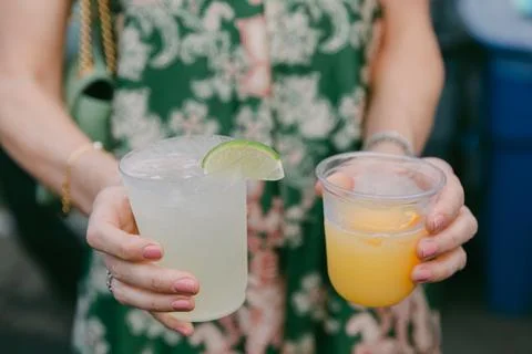 Refreshing drinks held in hands at a vibrant outdoor gathering during warm sunny Stock Photos