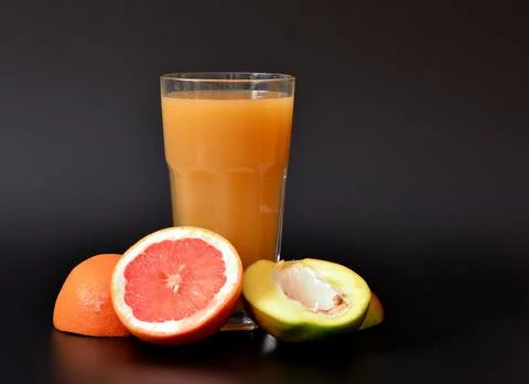 Refreshing fruit juice on a black background, next to the halves of ripe ma.. Stock Photos