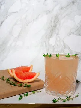 Refreshing grapefruit mocktail with ice and thyme on a marble background. Stock Photos