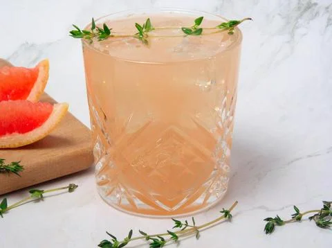 Refreshing grapefruit mocktail with ice and thyme on a marble background. Stock Photos