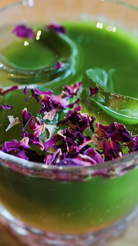 A refreshing green drink with ice cubes and delicate pink rose petals slowl.. Stock Footage 339342381