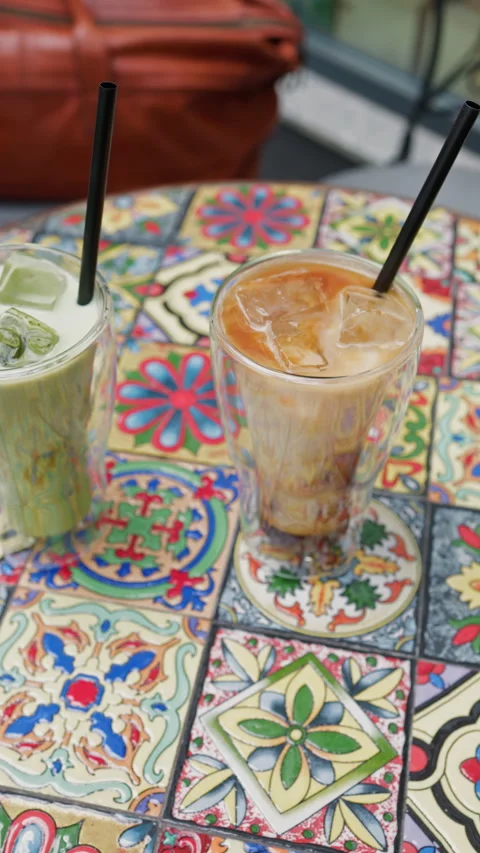 Refreshing iced beverages in clear glasses with black straws on colorful mosaic Stock Footage 337648404