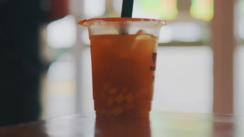 Refreshing Iced Fruit Tea in Plastic Cup with Straw on Wooden Table, Bokeh Stock Footage 333321688