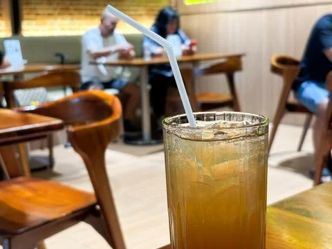 Refreshing Iced Tea with Straw in a Cozy Restaurant Interior Background Foto stock