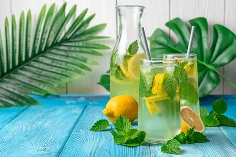 Refreshing lemonade with ice and mint on a light background with palm leaves. Stock Photos