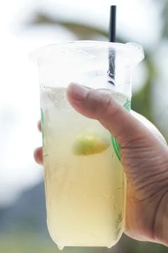 Refreshing Lemonade in Plastic Cup with Ice and Straw, Hand Holding Cold Dr.. Fotos de archivo