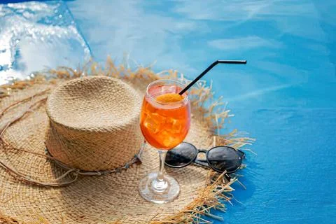 Refreshing orange drink with straw on poolside with hat Stock Photos