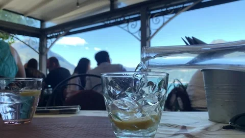 Refreshing Outdoor Dining: Water Pouring into Glass at Sky-View Restaurant Stock Footage 247999922