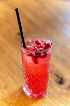 Refreshing raspberry cocktail with ice and black straw on wooden table Foto stock