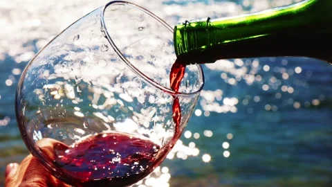 Refreshing red wine being poured into a glass by the water under bright sunlight Stock Footage 310996358