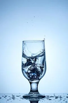 Refreshing splash of ice in a crystal-clear glass under serene blue backdrop Stock Photos