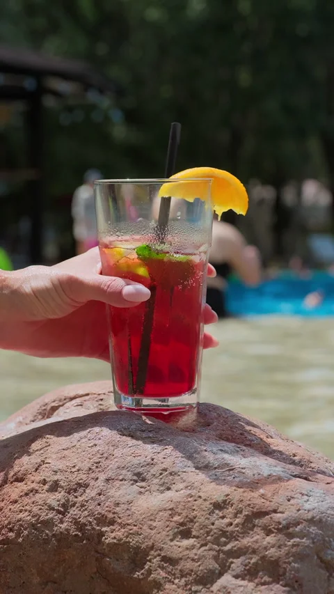 Refreshing summer cocktail orange slice rests on a rock near a pool. Summer Stock Footage 313740951