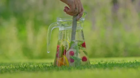 Refreshing summer drink with berries and citrus in a glass jug stirred outd.. Video stock 334930886