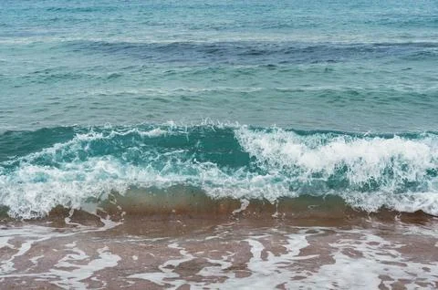 A refreshing wave crashes on a sandy beach, showcasing the serene beauty of a Stock Photos