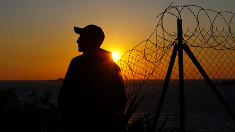 Refugee observing sunset behind barbed wire fence Stock Footage 302624615