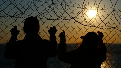 Refugees looking at sunset behind barbed wire fence Vídeo Stock 302625813
