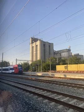 Regional passenger train on the tracks next to concrete silos of grain elevator Stock Photos