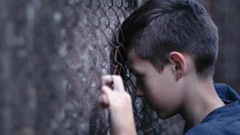 Regretful Reflection: Sad Boy Leaning Against Iron Fence, Contemplating Past Video stock 247453958