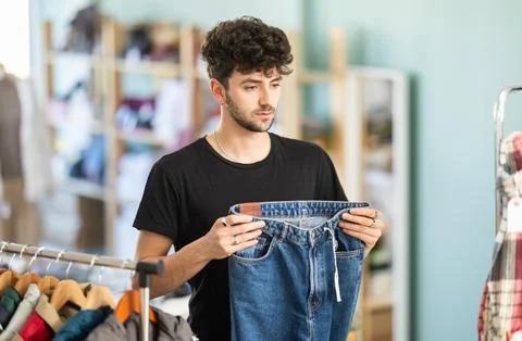 Regular customer guy chooses color and style of jeans trousers Stock Photos