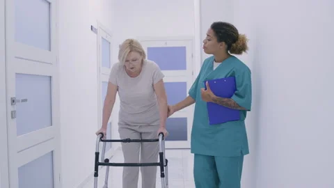 Rehabilitation after disease doctor helping weak female patient walk clinic hall Stock Footage