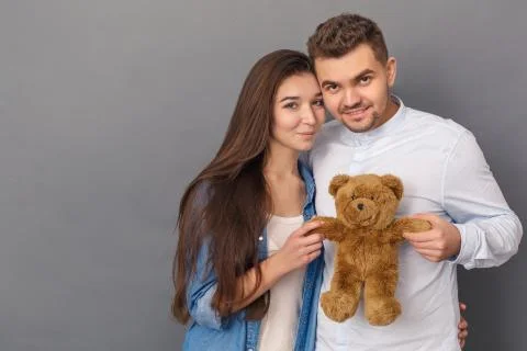 Relationship Concept. Young couple studio standing isolated on grey with teddy Stock Photos