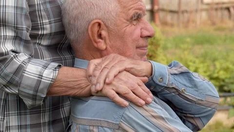 Relative puts hand on shoulder of elderly man who is sick and sitting in park Video stock 287724923