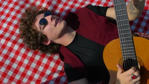 Relax at park - young man lying on the lawn plays guitar and his friend sings Stock Footage 154168757