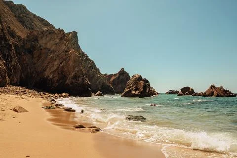 Relax on sandy beach while waves hit rocks during sunny day at coastal locati Stock Photos