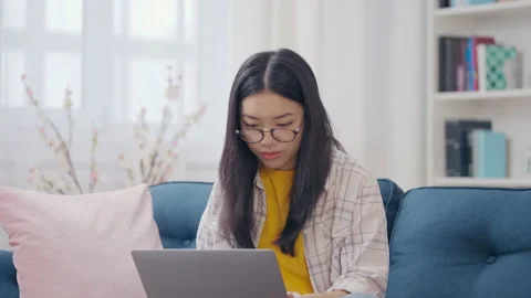 Relaxed Asian female programmer typing on laptop on couch, distance work, IT 스톡 동영상 197271033