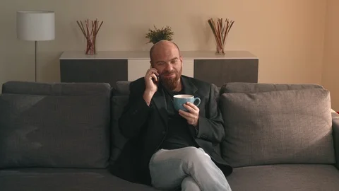 Relaxed bald man sitting sofa talking by phone drinking cup of tea Stock Footage 108382516