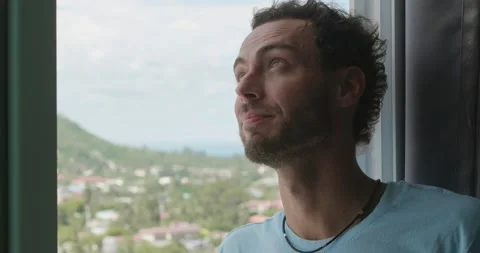 Relaxed bearded Caucasian man looking out the window overlooking the amazing Stock Footage 219950253