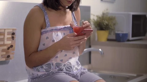 Relaxed beautiful brunette using smartphone, drinking orange juice-slow motion Video stock 104974763