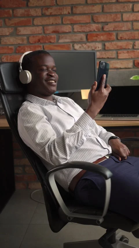 Relaxed black man at office using mobile phone and listening music Video stock 225442061