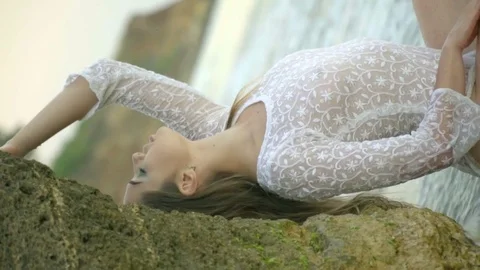A relaxed blonde with long hair in a translucent white dress sits at the edge of Stock Footage
