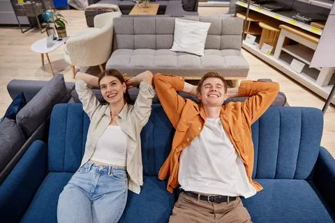 Relaxed couple sitting on sofa testing comfort of furniture at store Stock Photos