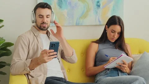Relaxed couple on yellow couch using smartphone and notebook during calm home Stock Footage 347056260