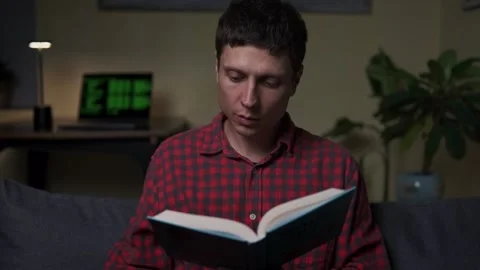 Relaxed evening reading, young man enjoying book, cozy lifestyle at home Stock Footage 318158528